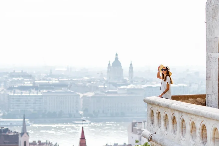 A woman on a white balustrade of Fisherman's Bastion in morning mist, with the dome of Parliament faint across the river